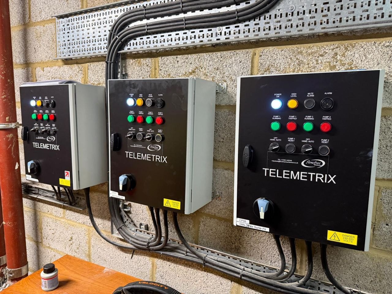 Three Telemetrix control panels installed side by side on a brick wall, wired and labelled